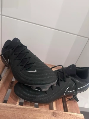 Nike Phantom fotbollskor - Snygga svarta Nike Phantom fotbollsskor med diskreta silverdetaljer och klassisk snörning. Storlek 43 HELT NYA asså aldrig använda! Köpte de som ett backup-par till mina andra som jag fäst mig vid. Men en otrolig doja denna med! Helt fräsha nya med box! Tror nypris kanske ligger runt 2000kr? Osäker buda ni utropspris kring 1500kr iallafall 