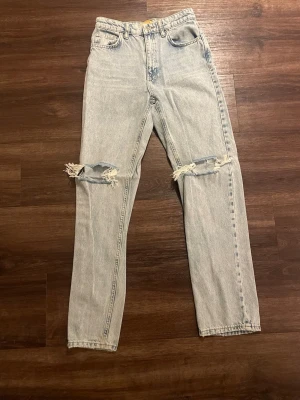 Ljusblå ripped jeans med raka ben - Säljer ett par ljusblå jeans med raka ben och slitna hål över båda knäna. Klassisk femficksmodell med hög midja och dragkedja. Perfekta för en avslappnad och trendig look. Jeansen är i storlek 164 för barn men är som storlek 32.💕🥰