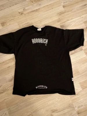 Svart HOODRICH t-shirt med tryck - Säljer en svart t-shirt från HOODRICH med vit logga tryckt på bröstet och ett större tryck på ryggen. 