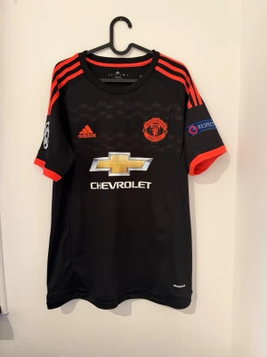 Manchester United bortatröja Adidas - Säljer en svart Manchester United bortatröja från Adidas med röda detaljer och tryck. Tröjan har Chevrolet-logga på bröstet, Champions League-märke på ärmen och Memphis Depay nummer 7 på ryggen. Tillverkad i lätt och ventilerande material.