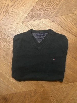 Mörkgrön stickad tröja Tommy Hilfiger - Snygg mörkgrön stickad tröja från Tommy Hilfiger med V-ringning och diskret logga på bröstet. Tröjan har långa ärmar och ribbade muddar vid ärmslut och nederkant. Perfekt till lager på lager och enkel att matcha.