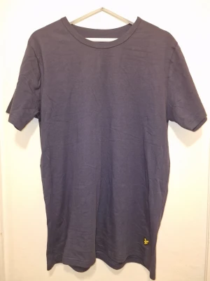 Marinblå t-shirt från Lyle & Scott - En stilren mörkblå t-shirt från Lyle & Scott med klassisk passform och loggan vid vänster kant. Perfekt till jeans eller shorts för en enkel och snygg look.