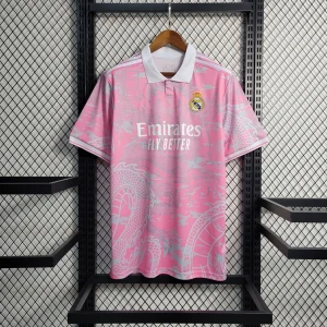 Rosa Real Madrid t-shirt med krage - Snygg rosa t-shirt från Real Madrid med vit krage och tryckt klubbmärke på bröstet. T-shirten har korta ärmar, subtilt mönster och vit logga framtill. Perfekt för dig som gillar sportig stil och vill sticka ut med färg.