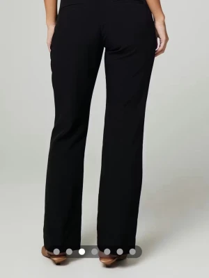 Svarta kostymbyxor bootcut - Snygga svarta kostymbyxor med bootcut passform och pressveck framtill. Byxorna har fickor i sidorna och hällor för skärp. Perfekta för en clean och stilren look. Materialet ser ut att vara en mjuk och följsam mix, troligen polyester eller viskos.