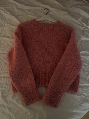 Rosa stickad tröja från H&M - Mysig rosa stickad tröja från H&M i ull- och alpackablandning. Tröjan har en rak passform, rund halsringning och ribbade muddar vid ärmslut och nederkant. Perfekt för kalla dagar och ger en söt och trendig look.