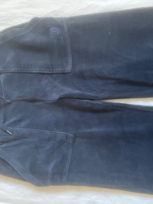 Mörkblå mjukisbyxor med fickor - Säljer ett par mörkblå mjukisbyxor med raka ben och stora fickor framtill. Byxorna har dragsko i midjan och är gjorda i ett mjukt, fleeceliknande material. Perfekta för chill dagar hemma eller när du vill vara extra bekväm.