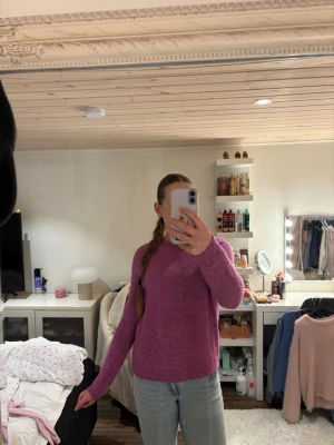 Lila stickad tröja med rund hals - Mysig lila stickad tröja med rund hals och långa ärmar. Tröjan har en enkel design utan mönster och är tillverkad i ett mjukt, fluffigt material som känns skönt mot huden. Perfekt att dra på sig när det är kyligt ute.