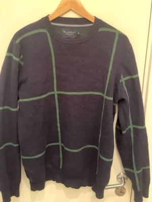 Mörkblå stickad tröja  M•Q  - Mörkblå stickad tröja från  M•Q med grönt rutmönster. Tröjan har rund halsringning och långa ärmar. Klassisk och stilren design som passar perfekt till vardagslooken. Materialet känns mjukt och bekvämt.