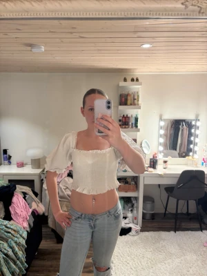 Vit croppad blus med puffärmar - Superfin vit blus med croppad passform och puffiga korta ärmar. Smockad överdel och volangkant nedtill ger en söt och trendig look. Perfekt att styla med jeans eller kjol för en fräsch outfit.