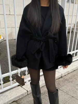 Svart kappa med fuskpälsdetaljer - Stilren svart kappa med knytskärp i midjan och breda ärmar med lyxiga päls armar vid ärmsluten. Perfekt för dig som vill ha en trendig och elegant look utan slitningar o defekter, den har även gömda fickor på båda sidor💗Tyvärr står det inte vart kappan är ifrån men skulle tro att den är från furr Stockholm då de ser exakt likadana ut!tveka inte med frågor osv💕