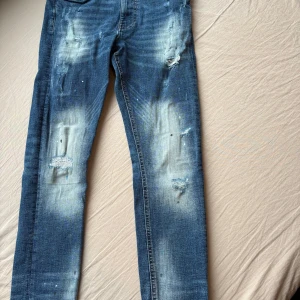 Blå slitna skinny jeans med detaljer från supply & Demand  - Säljer ett par blå skinny jeans med slitningar och ljusa tvättade partier. Jeansen har coola detaljer som hål och lagningar framtill, samt klassiska bakfickor. Perfekta för en avslappnad streetstil.