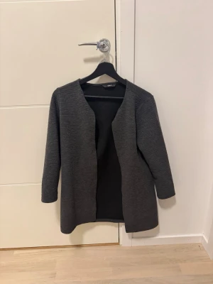 Mörkgrå öppen kappa från ONLY - Stilren mörkgrå kappa/kofta  från ONLY i öppen modell utan knappar. Kappan har en rak passform, trekvartsärmar och är tillverkad i ett mjukt, ribbat tyg. Perfekt för lager på lager och enkel att matcha med olika outfits.