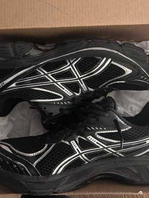 Svarta Asics GT-2160 sneakers - Säljer ett par svarta Asics GT-2160 sneakers med silvriga detaljer och mesh-överdel. Skorna har snörning och en platt sula som ger skön komfort. Perfekta för dig som gillar sportig stil och vill ha ett par snygga och funktionella sneakers.