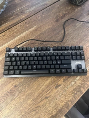 ZON Home of Victory tangentbord - Säljer ett svart mekaniskt tangentbord från ZON, modell Home of Victory. Tangentbordet har en klassisk rektangulär form och ansluts med kabel. Perfekt för gaming eller skrivbordsarbete. Färg: mörk/svart. Levereras i originalkartong.