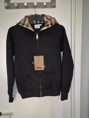 Svart Burberry hoodie med rutmönstrad huva - Burrberry zipp passar kroppslängden 165cm och bröst vidden 88 jag är 179 cm och den va inte så liten men ja rekommendera den till dem som är mellan 165-170 den är helt ny med prisstaggen kvar
