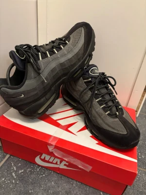 Nike Air Max 95 svarta/grå sneakers - Nike Air Max 95 sneakers i svart och grått med mesh och mockadetaljer. Klassisk chunky sula med synliga Air-enheter och reflekterande detaljer. Snygga snören och ikonisk design som sticker ut. Perfekta för dig som gillar streetwear och sportig stil. Skick 7/10👌