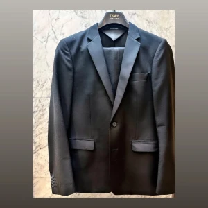 Kostym Tiger of Sweden storlek 48 - Kostym med diskreta smokinginfluenser, klädda slag och revärer. Modellen är ”Smiths Tux”. Fint skick, använd få gånger. Ett pyttelitet, nästan osynligt, hål inne vid armvecket på baksidan av höger ärm (se bild). Kan lätt lagas, hålet är minimalt.