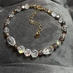 Pärlarmband med diamantformade pärlor och guldiga hjärtan och spänne. Justerbar passform mellan 19-25 cm.