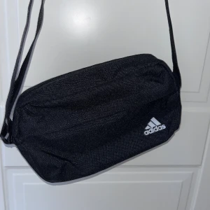 Adidas midjeväska - I bra skick! Går att justera längd på bandet! Yttreficka samt innerficka i ”vanliga” fickan. 