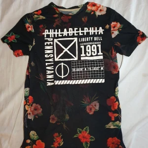 Somrig T-shirt (Storlek xs/s) - Håller på rensa garderoben lite från kläder som bara ligger, Otroligt snygg t-shirt med blommor och ett tryck. Detta har varit en favorit t-shirt men tyvärr så är den för liten nu. Gammal men i bra skick lite nopprig.