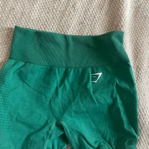 Gröna träningsshorts - Ett par gröna träningsshorts med hög midja och elastisk linning. Shortsen är tillverkade i ett stretchigt material och har en åtsittande passform. använda ca 2 ggr