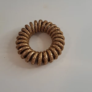 Guldfärgad hårslips - En guldfärgad hårslips med en spiralformad design. Det har en glittrig yta som ger ett elegant och festligt utseende.