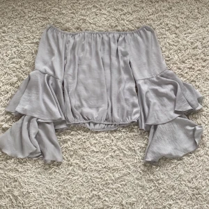 Ljusgrå offshoulder topp från BikBok - En ljusgrå offshoulder topp från BikBok i storlek XS. Toppen har långa ärmar med volangdetaljer och en elastisk kant vid midjan och axlarna för en bekväm passform.