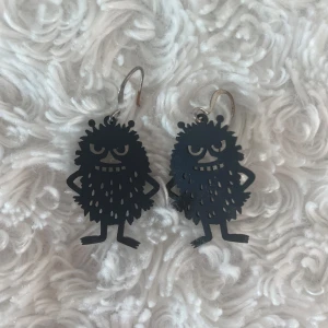 Örhängen Mumin Stinky - Muminörhängen. Svarta i gummiliknande material med hängen i metall. Använda någon enstaka gång. 