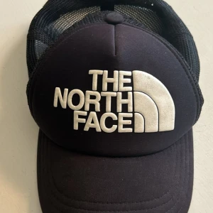 Svart keps från The North Face - En svart keps från The North Face med vit logotyp på framsidan. Kepsen har en böjd skärm och ett nätmaterial på baksidan för ventilation.