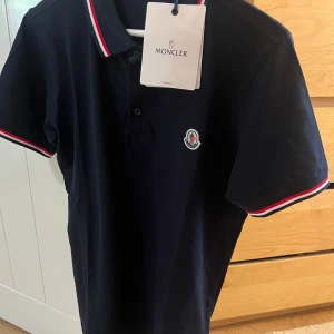Moncler Piké  - Säljer denna snygga pikén som passar sjukt bra för sommaren. Färgen är mörk blå och skicken på piken är 10/10. Storleken är L men dock passar den som ett M. Hör av dig om du är intresserad för och köpa eller byta!!