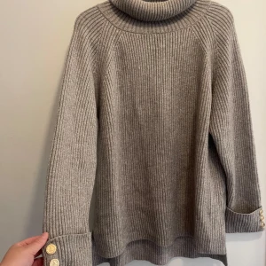 Stickad tröja i Grå/ Silver  - Stickad tröja i Grå/ Silver med lite Skimmer/ glitter i sig. Det är riktigt fint och bra kvalitet på tyget, tyngre tyg.  Lite längre modell. Har liten krage. Guldiga knappar Använd kanske 3 gånger Storlek: S