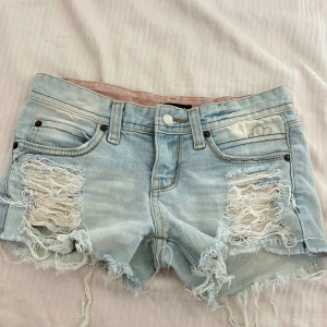 Ljusa jeansshorts med slitningar - Ett par ljusa jeansshorts med slitningar och fransiga kanter. Shortsen har fem fickor och bälteshällor.