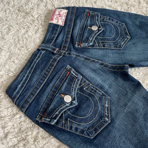 Vintage True Religion jeans - I behov av pengar säljer jag mina favvojeans. 🥲 Lågmidjad och bootcut modell med snygga detaljer. De är i nyskick, förutom att de är uppsydda längst ner. ❤️ Innerben: 78cm, midja rakt över: 36cm. Jag är 167. 🫶 Fler vintage jeans finns på min profil. 🥰