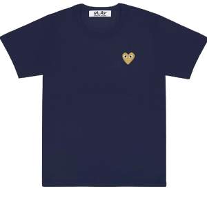 Jättefin T-Shirt från Comme des Garçons. T-shirten är marinblå med ett guldigt hjärta. Tröjan är i bra skick o använd få gånger. Skriv för fler bilder!