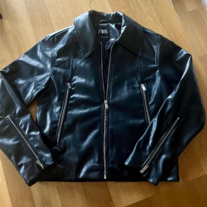 Skinnjacka med dragkedjor.  - Imitations skinnjacka i nyskick. Fickor fram med dragkedjor. Dragkedjor på ärmarna med krage. Nypris 699kr. 