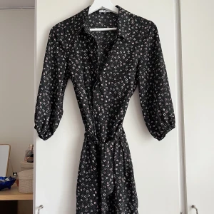 Skjortklänning - Blommig skjortklänning med trekvartsärmar. Knäppning hela vägen, smalt skärp i midjan. Använd fåtal gånger, så mycket gott skick! Stl 34, men passar lika bra på 36. 