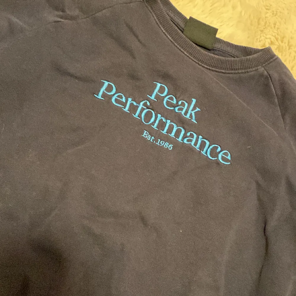 En mörkblå sweater från peak performance med ljusblå text i mitten. . Hoodies.