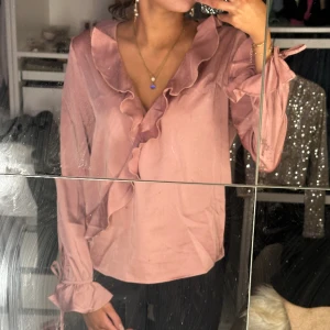 Rosa blus - Rosa blus med volanger och knytning i ärmarna. Knapp i mitten vid brösten som gör att den inte glider ner osv. Använd fåtal gånger. 