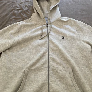 Polo Ralph Lauren Zipper grå  - Hej, jag säljer min Polo Ralph Lauren Zipper. Den är köpt i USA, har ej kvitto. Tröjan är 9/10 skick och inga deflekter!!!. Tröjan har bara få tal användningar. Jag säljer den för att den inte passade mig. KAN BYTA MOT S I SAMMA MODEL.