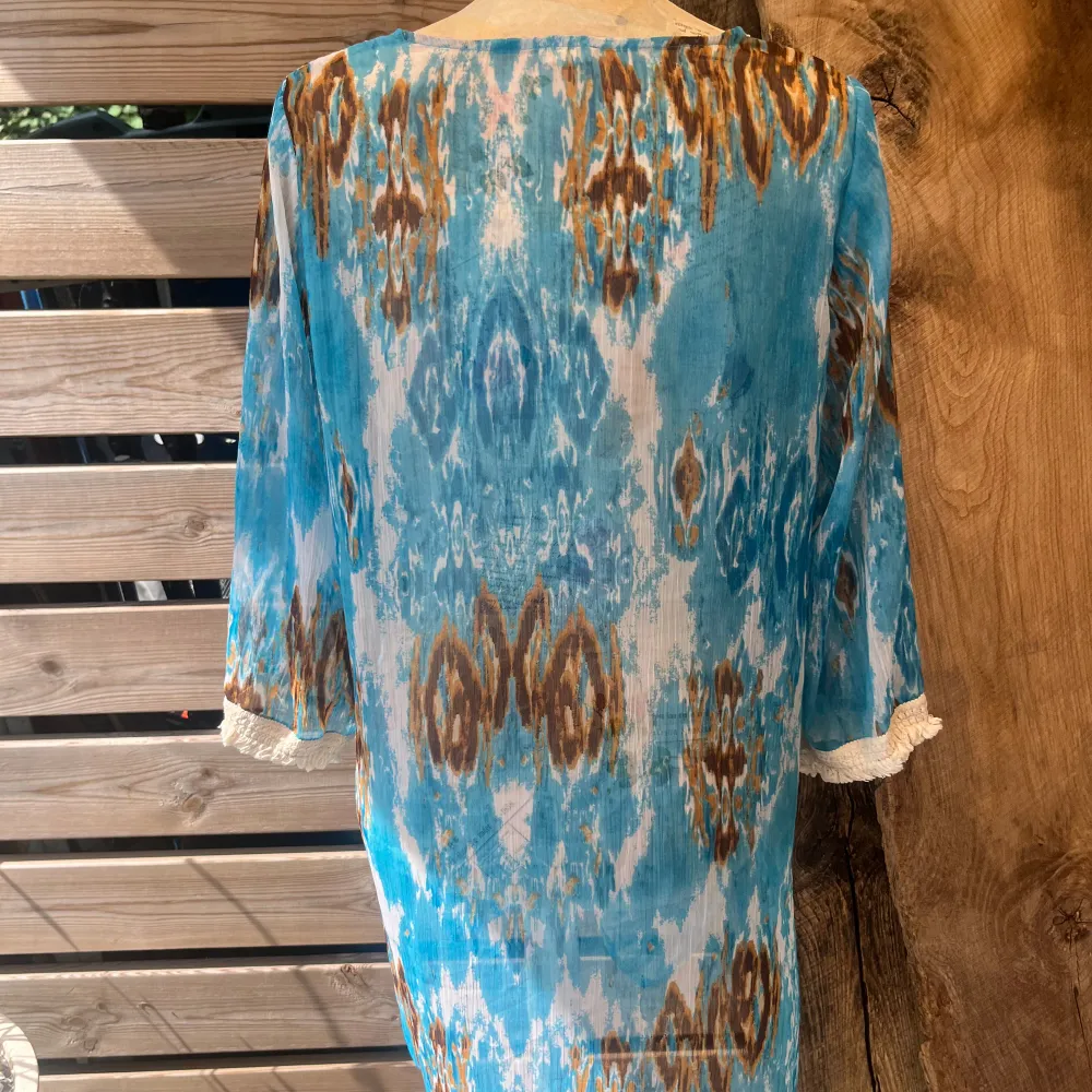 Härlig tunika/blus/strandklänning i vitt, turkosblå, brunt batik mönster som är väldigt skirt/luftigt samt vackra detaljer i byst och ärmslut som är virkade. Fint skick! Stl M . Blusar.