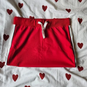 Röd minikjol i mjukismaterial - En röd miniskirt med vita ränder på sidorna, i mjukismaterial och därav väldigt skön. Passar XS till M och aldrig använd. I fint skick. Skriv vid prisförslag eller frågor. Kan skicka fler bilder.