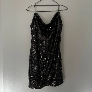 Svart paljettklänning  - Paljettklänning i svart, storlek 38. Waterfall effekt i bysten. Korsade band i ryggen.  Använd en gång 