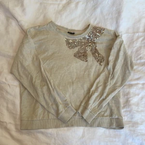 Tröja med paljetter - Tröja med paljetter i form av en rosett från Kappahl. Väldigt bra skick. Använd förr men nu för liten. Är stor i storleken så den passar på folk som har storlek s också❤️