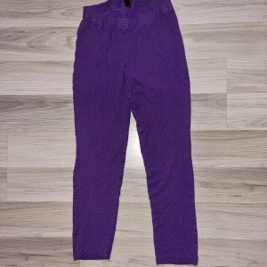 Lila leggings  - Ett par lila leggings med en tight passform. Leggings har en elastisk midja och är tillverkade i ett texturerat material. Från m i stl 140