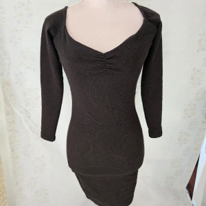 Svart klänning från NLY Trend - En elegant svart klänning från NLY Trend i storlek S. Klänningen har en åtsittande passform med långa ärmar och en v-ringad hals. Materialet har en subtil textur som ger en extra dimension till plagget.