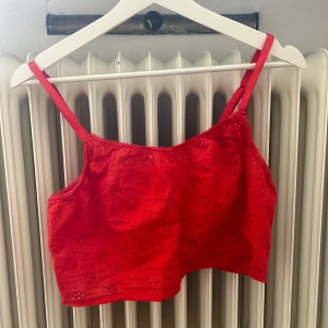 Röd broderad linnetopp - En röd linnetopp med broderade blommor och smala axelband. Toppen är kort och har en somrig design.