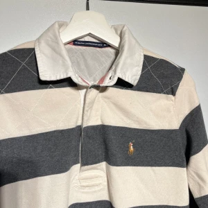 Ralp lauren polotröja  - Riktigt fräsch långärmad polo tröja från Ralp Lauren, även kallad rugbytröja. Står storlek m/m men passar ca XS. Använd men i mycket fint skick utan några skador eller defekter. Grå och krämvit randig