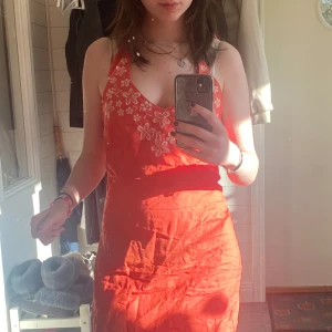  halterneckklänning  - Orange/rosa/korall klänning med vita blommor broderade på. Halterneck! I gott skick. 