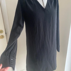 Svart klänning, stl 36 - Fin och skön svart klänning i rak modell och med långa armar. Fina detaljer på axlarna. Tunt material. Sparsamt använd och fint begagnat skick. Kommer från djur- och rökfritt hem. Passar både vardag och fest! 