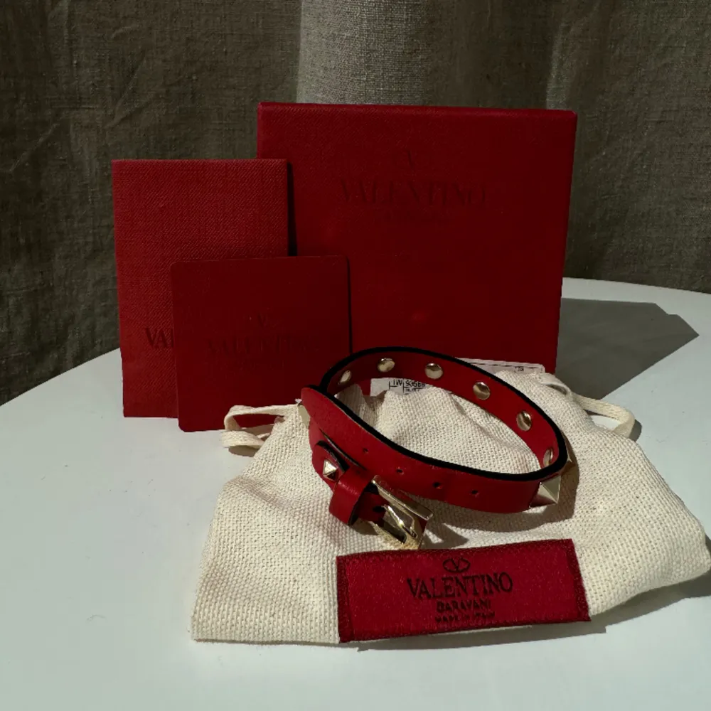 Rött valentino armband med guldiga nitar. Endast använt vid speciella tillfällen så fortfarande i väldigt fint skick. Originallådan med tillhörande lappar finns kvar. . Accessoarer.